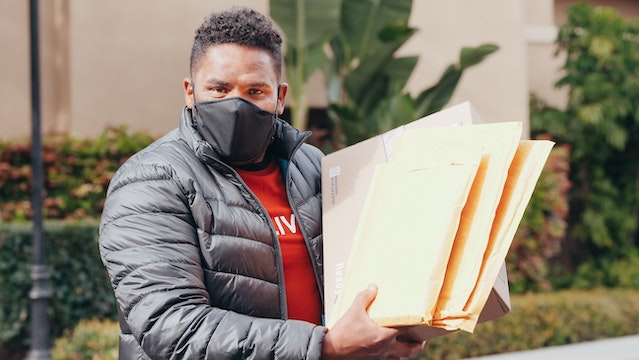Person wearing a mask and holding a handful of mail packages