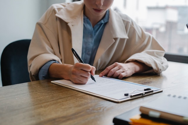 Person writing on a printed paper on a clipboard